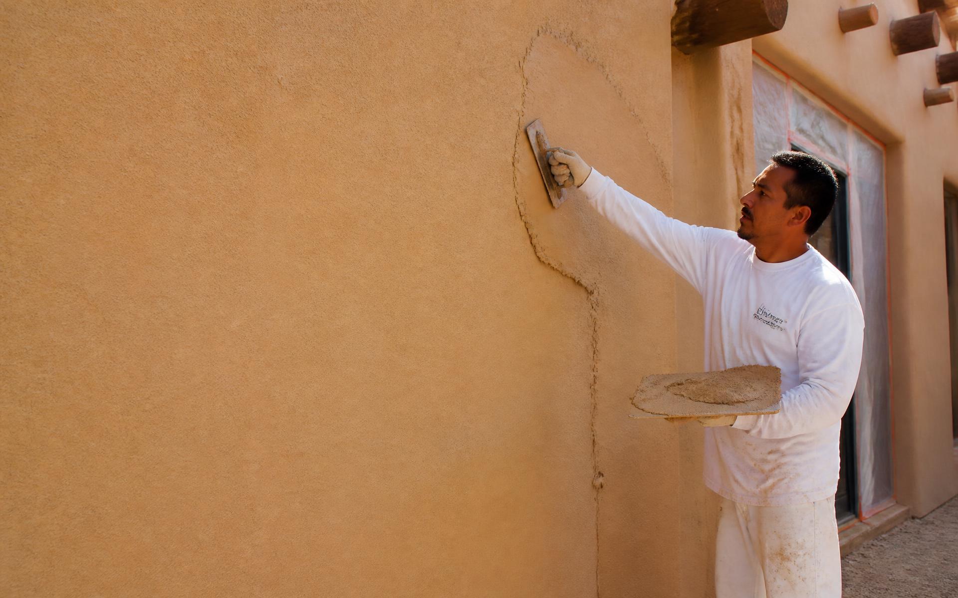 Stucco professional applying a sand finish coat to the exterior wall of a home