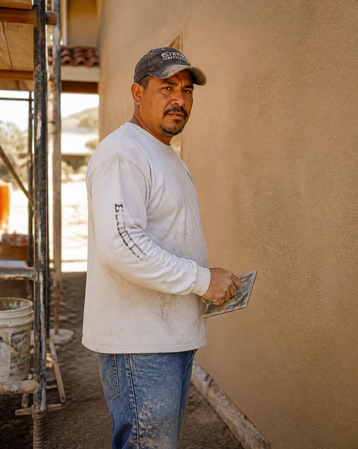 Emilio Lobos, owner of Lobos Stucco, at a jobsite beside a freshly finished stucco wall